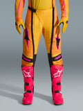 Alpinestars 2026 Techstar Nomur Hose, Motocross-Hose, Orange, Gelb und Pink, getragen mit passenden gelben Handschuhen und leuchtend pinkfarbenen Rennstiefeln, mit schwarzen Einsätzen und auffälligem pinkfarbenem Alpinestars-Branding, technische Offroad-Rennausrüstung