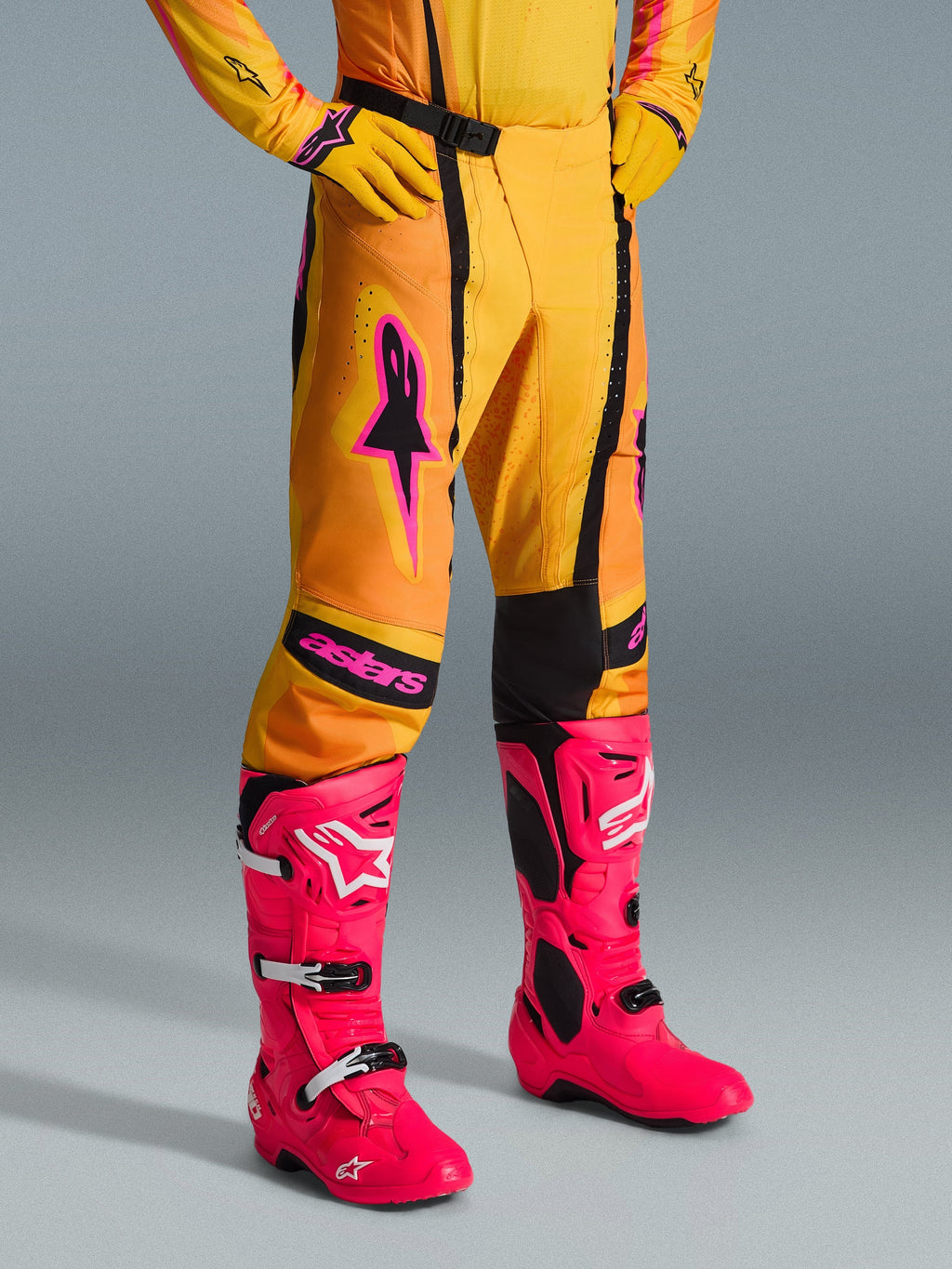 Alpinestars 2026 Techstar Nomur Hose, Motocross-Hose, Orange, Gelb und Pink, getragen mit passendem gelbem Jersey und Handschuhen sowie leuchtend pinkfarbenen Stiefeln, athletische Rennpassform mit pinkem Branding und schwarzer Magnetschnalle, lebhafte Ausrüstung für den Offroad-Wettbewerb