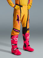 Alpinestars 2026 Techstar Nomur Hose, Motocross-Hose, Orange, Gelb und Pink, getragen mit passendem gelbem Jersey und Handschuhen sowie leuchtend pinkfarbenen Stiefeln, athletische Rennpassform mit pinkem Branding und schwarzer Magnetschnalle, lebhafte Ausrüstung für den Offroad-Wettbewerb