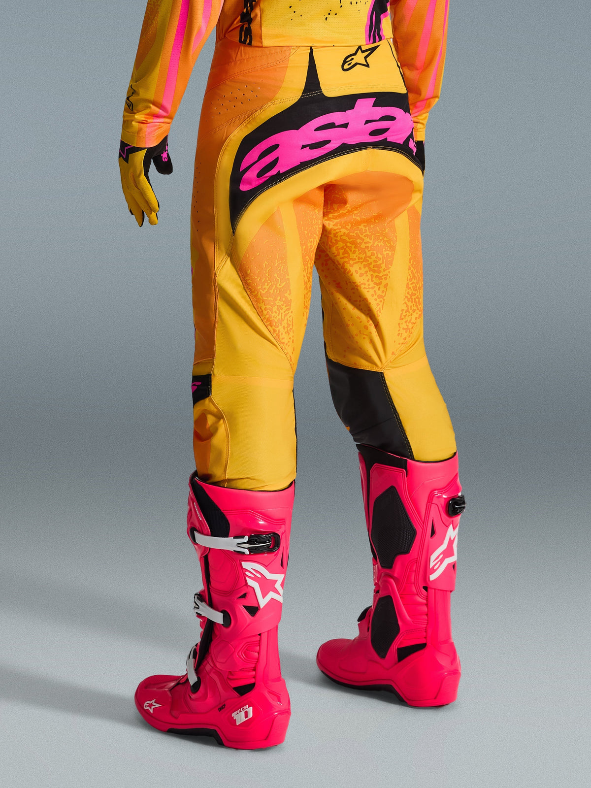 Alpinestars 2026 Techstar Nomur Hose, Motocross-Hose, Orange, Gelb und Pink, Rückansicht mit großem pinkem 'astars'-Branding auf der Sitzfläche, kombiniert mit leuchtend pinken Tech 10 Stiefeln und passendem Trikot, Performance-Rennausrüstung für Motocross