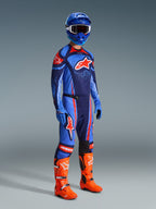 Alpinestars 2026 Techstar Nomur Pants, Motocross Pants, Dark Navy Orange and UCLA Blue, worn by a rider in complete racing gear including a matching jersey, blue helmet, and bright orange boots, performance-engineered for off-road racing
