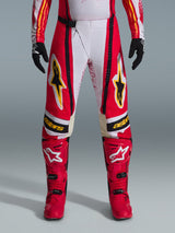 Pantalon Alpinestars Techstar Nomur 2026, pantalon de motocross, rouge et blanc avec des accents noirs et jaunes, porté avec des bottes rouges assorties et des gants noirs, équipement de course tout-terrain haute performance