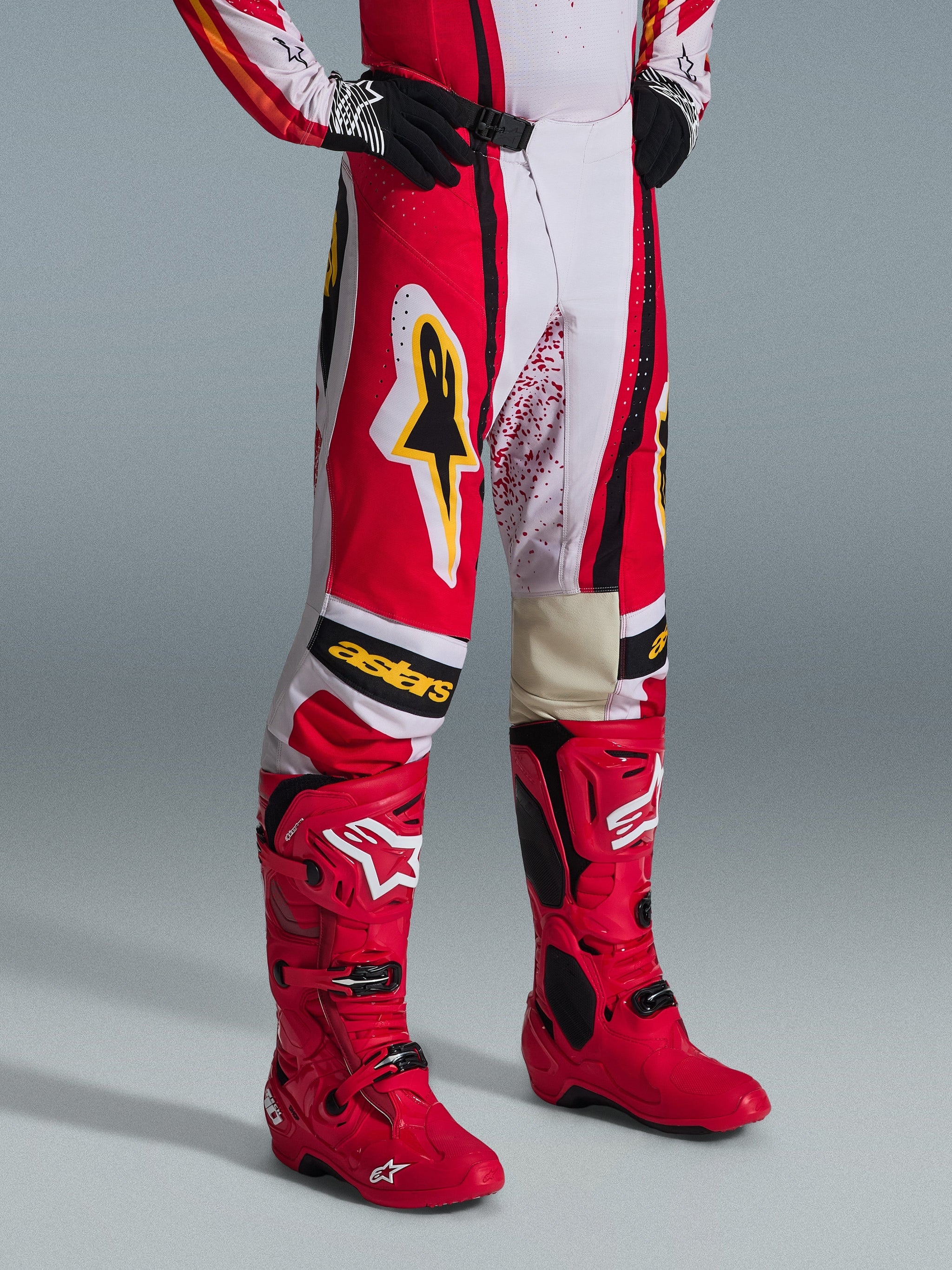Alpinestars 2026 Techstar Nomur Pants, pantalon de motocross, rouge, blanc et noir avec accents jaunes, porté avec des bottes de motocross rouges assorties et des gants noirs, arborant le logo Alpinestars jaune et le marquage « astars » sur les genoux, équipement de course tout-terrain professionnel