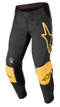 Alpinestars Techstar Quadro broek, motorcross off-road broek, zwart en geel met oranje accenten, groot geel sterlogo op de linkerdij, versterkte gele kniebescherming met zwarte logo's, ventilatieopeningen en een stevige ratelsluiting voor een high-performance racepasvorm.