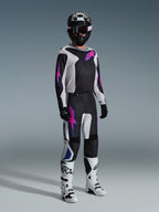Motocross rider wearing complete racing gear, Alpinestars 2026 Fluid Grid Pants in Black Light Gray and Purple, matching jersey with pink and blue graphics, black helmet and goggles, white and black boots, and black gloves, coordinated outfit for off-road racing