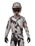 Alpinestars 2024 Racer Tactical Jersey, maillot de motocross, motif camouflage Iron Camo Dust Gray, pilote portant un casque et des lunettes assortis avec des gants noirs, équipement technique pour la course tout-terrain