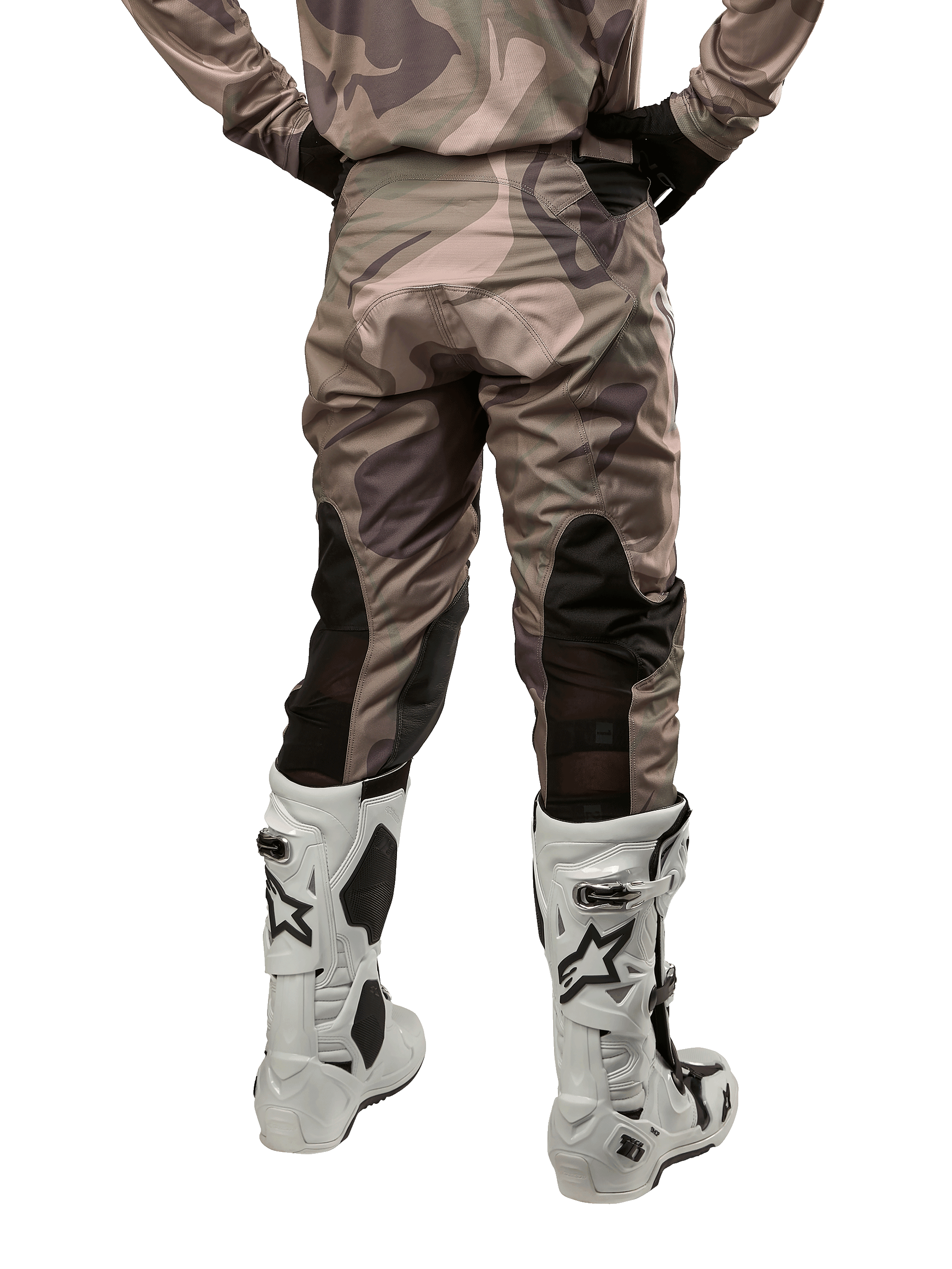 Alpinestars 2024 Racer Tactical Pants, pantalon de motocross, camouflage vert militaire et marron, vue arrière montrant le motif camouflage et les panneaux extensibles noirs respirants sur le bas des jambes, porté avec des bottes de motocross blanches, équipement technique durable pour la conduite tout-terrain
