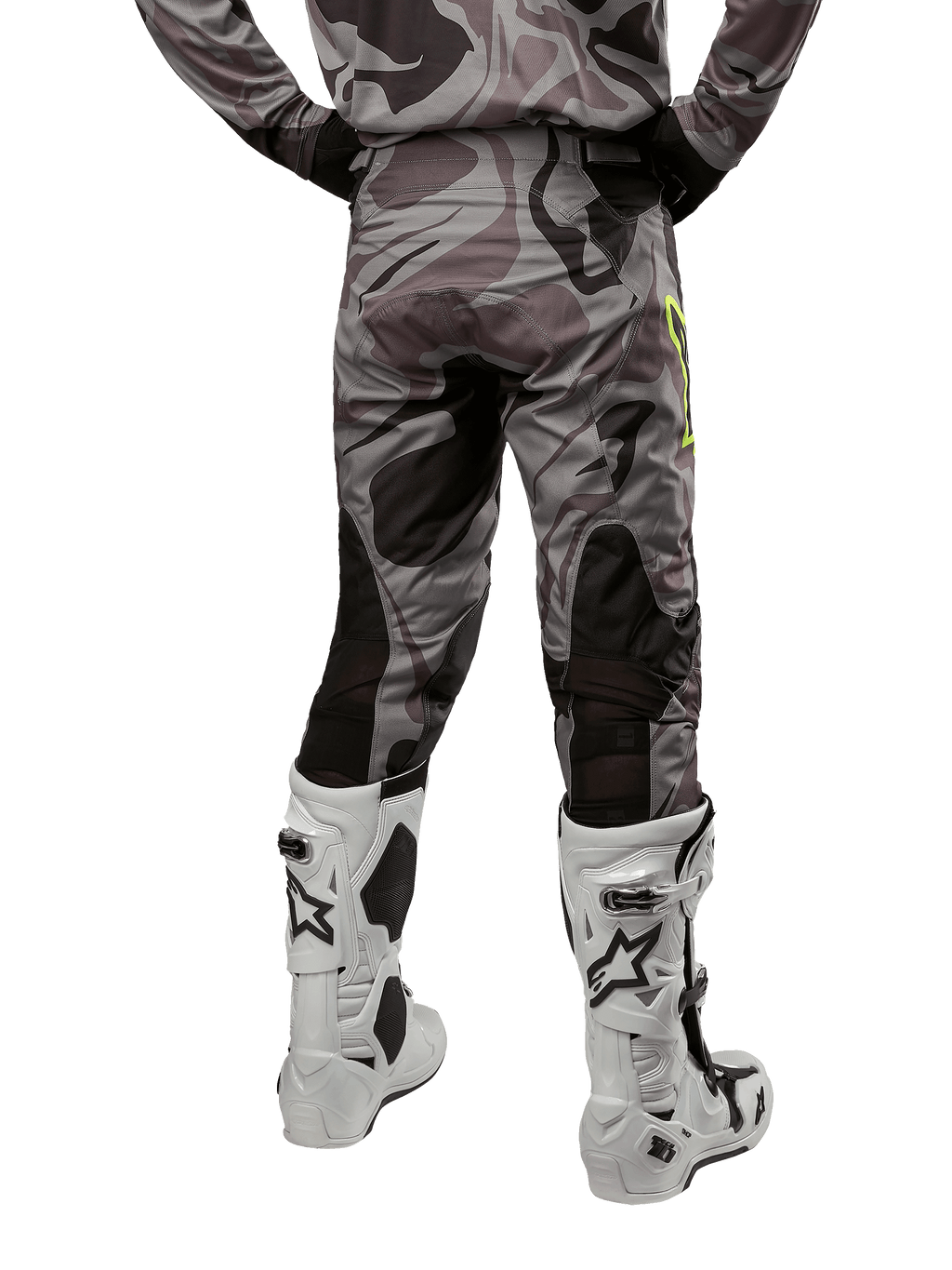 Alpinestars Pantalon Racer Tactical 2024, pantalon de motocross, Cast Gray Camo Magnet, vue arrière montrant le motif camouflage et les zones extensibles respirantes noires, porté avec des bottes de motocross blanches et noires, conçu pour la course tout-terrain