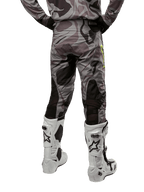 Alpinestars Pantalon Racer Tactical 2024, pantalon de motocross, Cast Gray Camo Magnet, vue arrière montrant le motif camouflage et les zones extensibles respirantes noires, porté avec des bottes de motocross blanches et noires, conçu pour la course tout-terrain