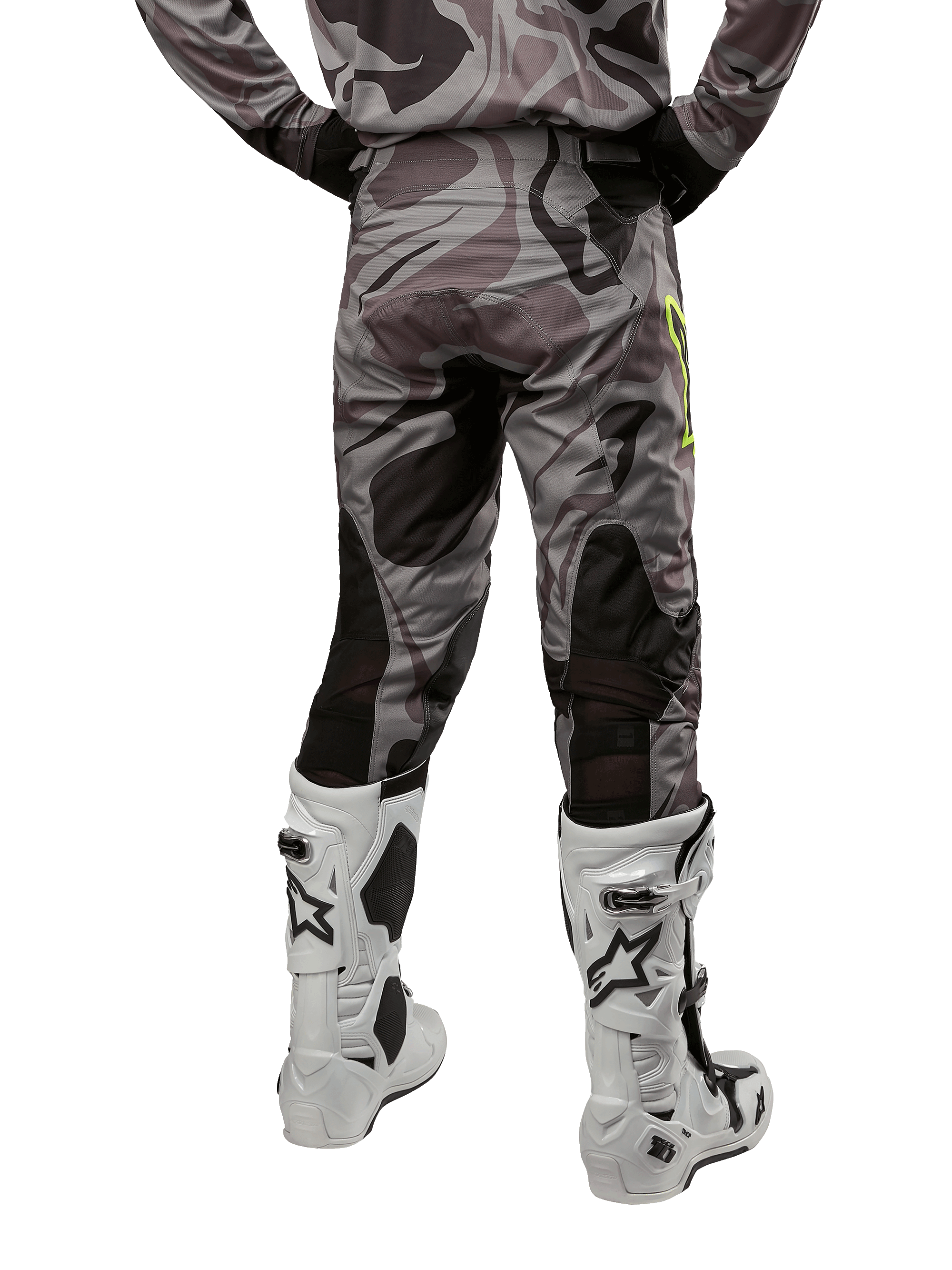 Alpinestars Pantalon Racer Tactical 2024, pantalon de motocross, Cast Gray Camo Magnet, vue arrière montrant le motif camouflage et les zones extensibles respirantes noires, porté avec des bottes de motocross blanches et noires, conçu pour la course tout-terrain