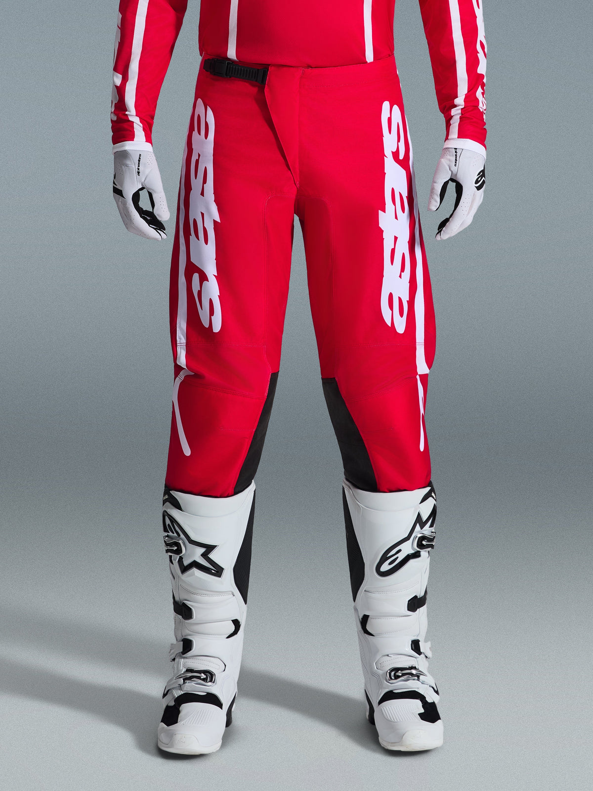 Alpinestars 2026 Fluid Apex Hose, Motocross-Hose, Rot und Weiß, mit großen weißen Astars-Logos auf den Oberschenkeln und schwarzen Knie-Innenpaneelen, getragen mit passenden weiß-schwarzen Stiefeln und Handschuhen für einen kompletten Offroad-Racing-Look.