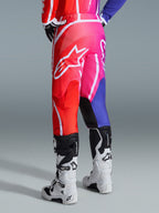 Alpinestars 2026 Fluid Apex Pants, Motocross Pants, Multicolor Red Pink and Purple, Rear view of rider wearing pants with white and black motocross boots, featuring large white Alpinestars logo, vibrant gradient design