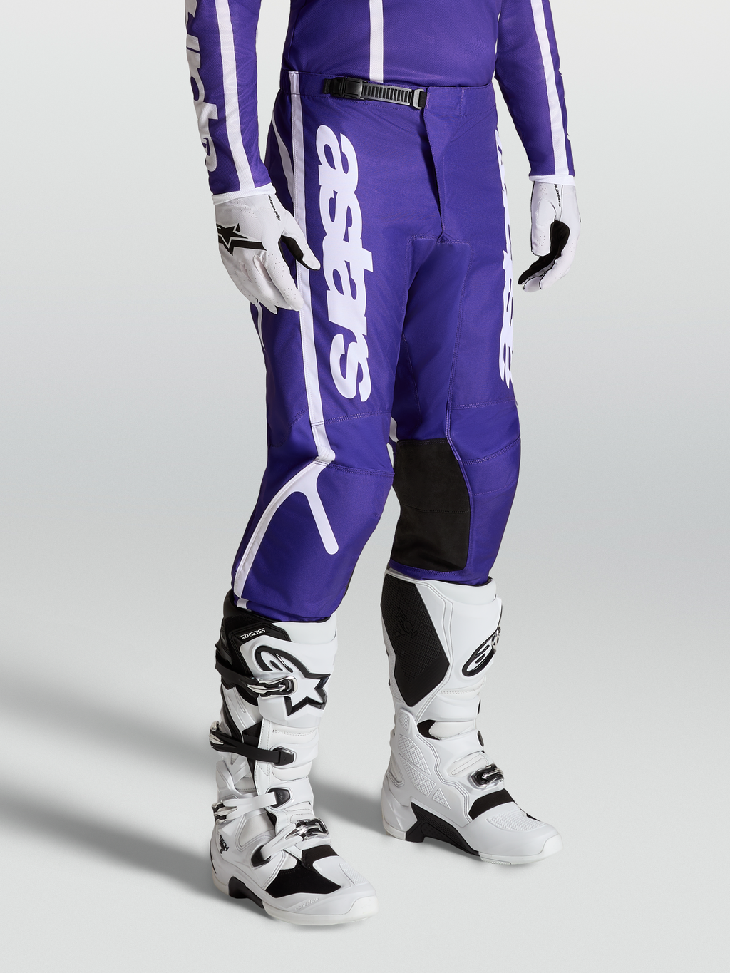 Alpinestars Pantalon Fluid Apex V2, équipement de motocross pour homme, bleu et blanc, jambes pré-courbées, porté avec bottes et gants blancs