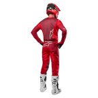 Pantalon et maillot assorti Alpinestars Racer Hoen 2024 en Mars Red Burgundy, vue arrière d'un pilote de motocross en tenue complète avec casque rouge et bottes blanches, illustrant la coupe athlétique et le marquage pour la course tout-terrain.