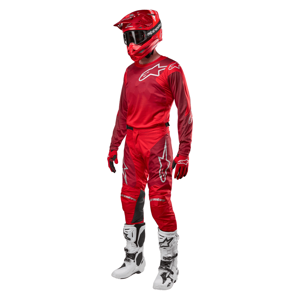 Pilote de motocross portant un équipement de course complet, pantalon et maillot Alpinestars Racer Hoen 2024 en Mars Red Burgundy, casque rouge, gants rouges et bottes blanches et noires, tenue coordonnée pour la course tout-terrain