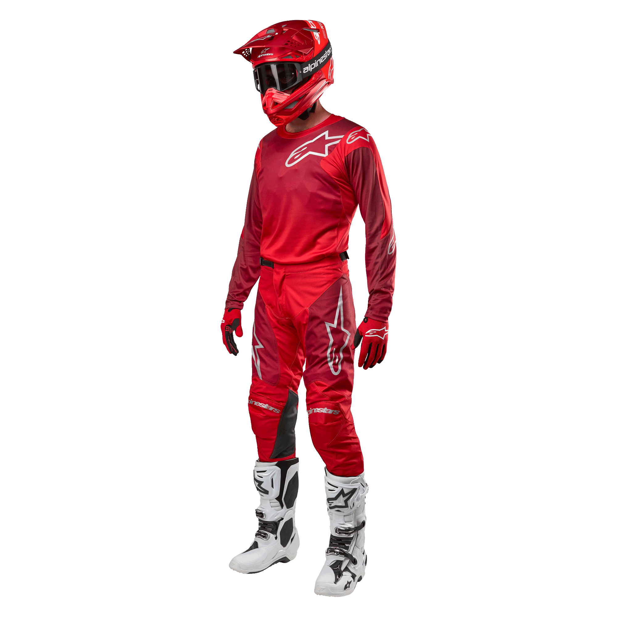 Pilote de motocross portant un équipement de course complet, pantalon et maillot Alpinestars Racer Hoen 2024 en Mars Red Burgundy, casque rouge, gants rouges et bottes blanches et noires, tenue coordonnée pour la course tout-terrain