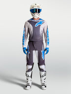 Alpinestars Fluid Drag broek en motocross gear set voor heren, grijs en blauw met bijpassende jersey en witte motorlaarzen, professionele off-road kleding.