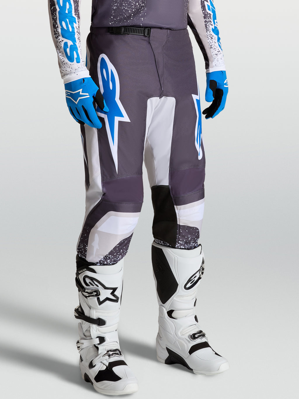 Alpinestars Fluid Drag broek, heren motorcrossbroek, grijs, lila en UCLA-blauw, ergonomische pasvorm, met witte laarzen.