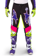 Alpinestars Limited Edition Supertech Dirt Studios Hose, Motocross-Hose, Weiß, Lila und Neongelb, mit schwarzen Einsätzen sowie neongelben und pinken Akzenten, große lila Stern-Logos, abgebildet mit passenden neongelben Handschuhen und lila Rennstiefeln, strapazierfähige Offroad-Rennbekleidung