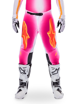Alpinestars Limited Edition Supertech AFD MIG Pants, motorcrossbroek, fluo roze en wit met oranje accenten, met grote sterlogo's op de bovenbenen, geperforeerde panelen en zwarte knie-gripzones, gedragen met witte en zwarte motorcrosslaarzen