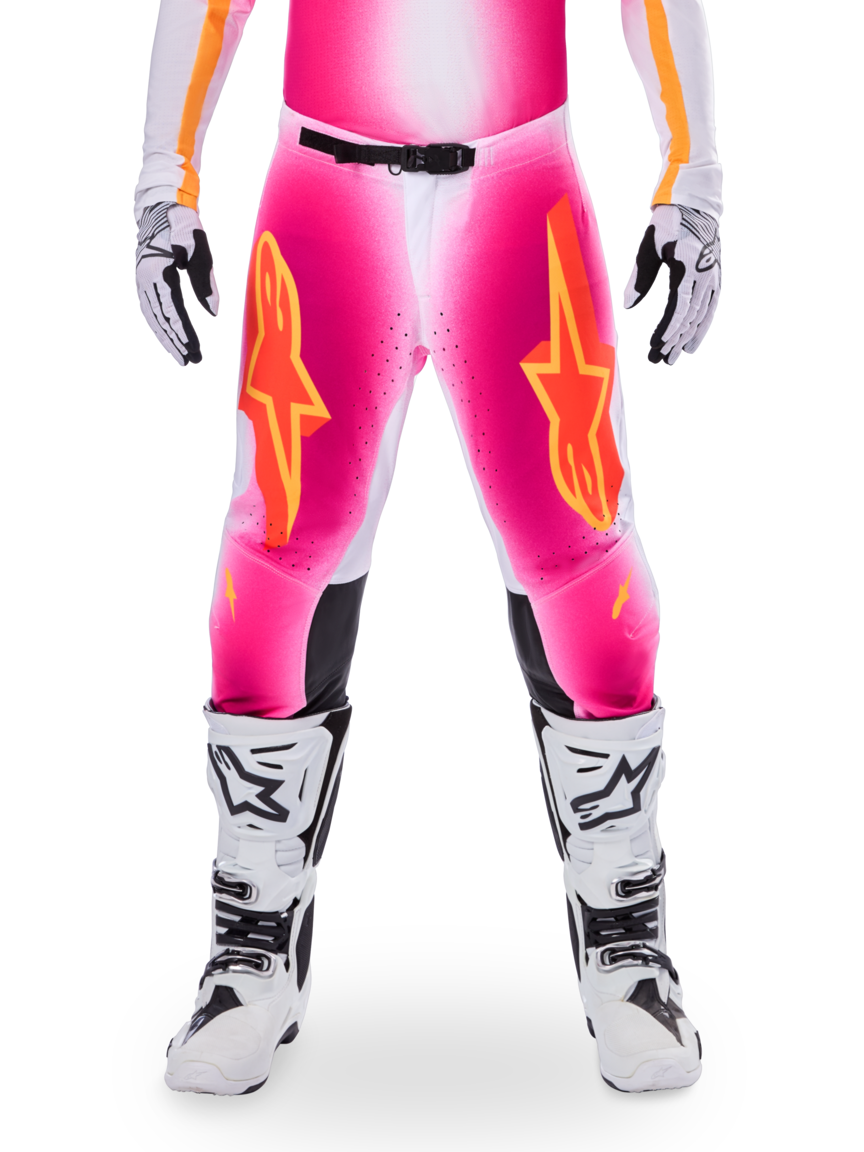 Alpinestars Limited Edition Supertech AFD MIG Hose, Motocross-Rennhose, Pink Fluo und Weiß mit orangen Akzenten, mit großen Stern-Logos auf den Oberschenkeln, perforierten Einsätzen und schwarzen Knie-Grip-Zonen, getragen mit weiß-schwarzen Motocross-Stiefeln
