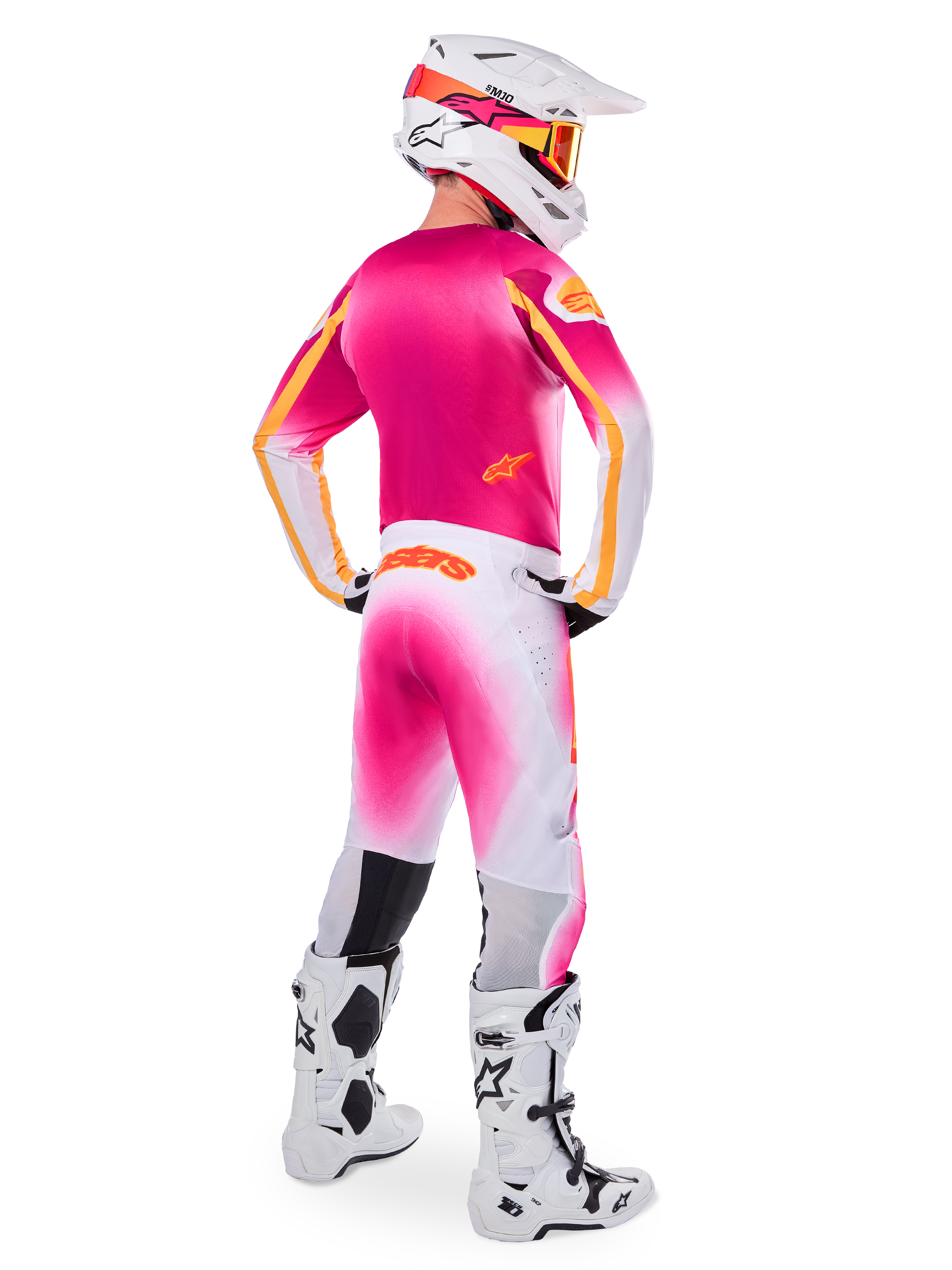Motocross-Fahrer in der Rückansicht, Limited Edition Supertech AFD MIG Gear Set, pinkes Trikot mit orangefarbenen Akzenten, weiße Hose mit pinkem Farbverlauf und orangefarbenem Alpinestars-Branding, weißer Helm mit pinken Grafiken und orangefarbener Brille, weiß-schwarze Stiefel, professionelle Offroad-Rennausrüstung