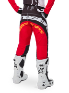 Alpinestars Limited Edition Techstar Deep Hose, Motocross-Hose, Schwarz, Weiß und High Red, Rückansicht mit markantem weißen Alpinestars-Logo auf dem Gesäß und orangefarbenem Branding, getragen mit weißen technischen Stiefeln für professionellen Offroad-Rennsport.