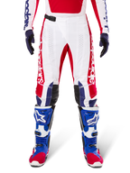 Alpinestars Limited Edition Techstar Fortitude Hose, Motocross-Hose, Hellrot, Weiß und Blau, getragen mit passender Ausrüstung einschließlich blauer Schutzstiefel und Handschuhe, weißes Chassis mit roten Grafiken, schwarze Leder-Knieeinsätze und lasergeschnittene Perforationen, professionelle Offroad-Rennbekleidung