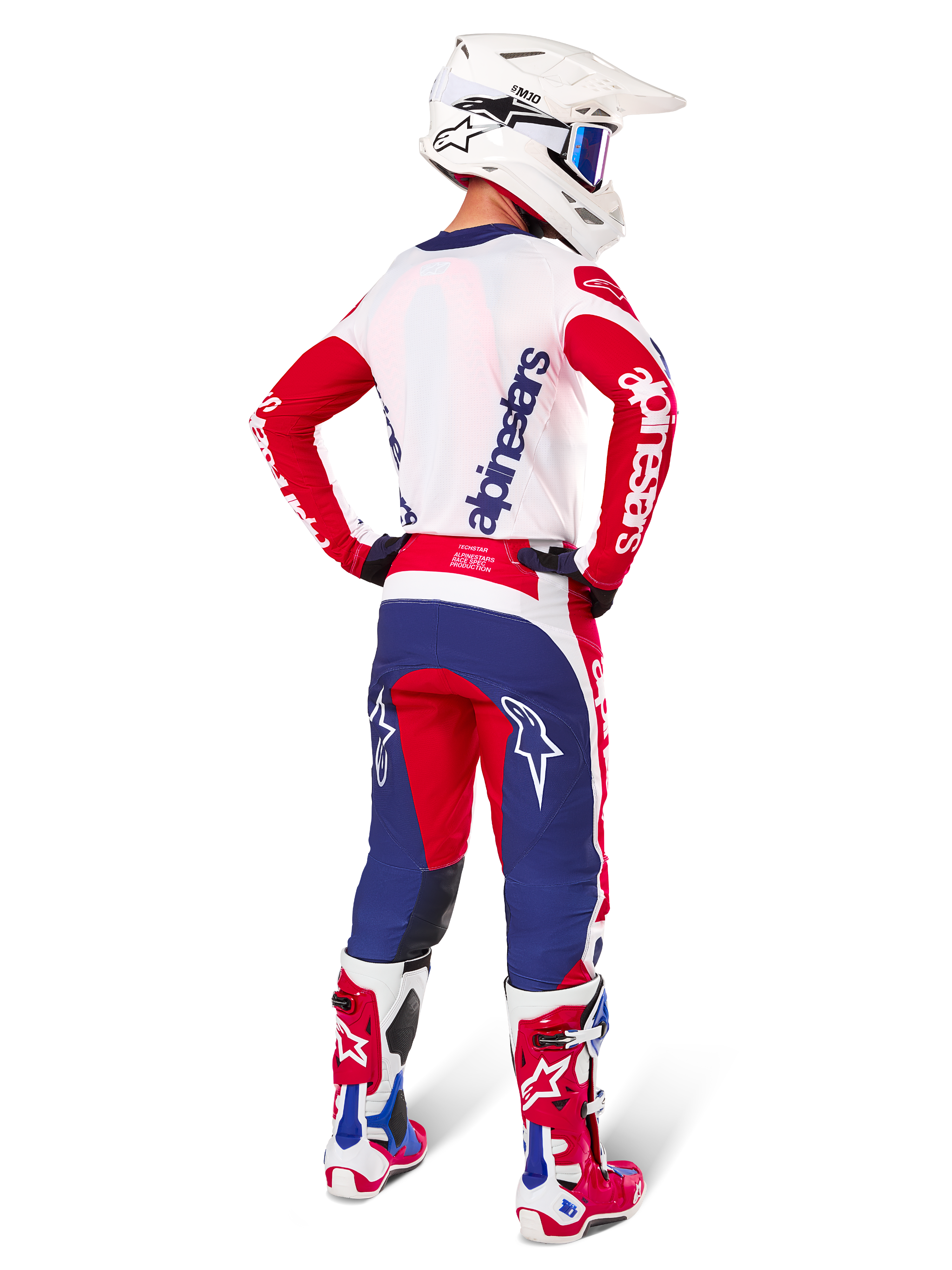 Alpinestars Limited Edition Techstar Fortitude Hose, Motocross-Hose, Hellrot, Weiß und Blau, in der Rückenansicht an einem Fahrer mit passendem Trikot, Stiefeln und Helm dargestellt, hebt die athletische Passform und die markante Logoplatzierung hervor.
