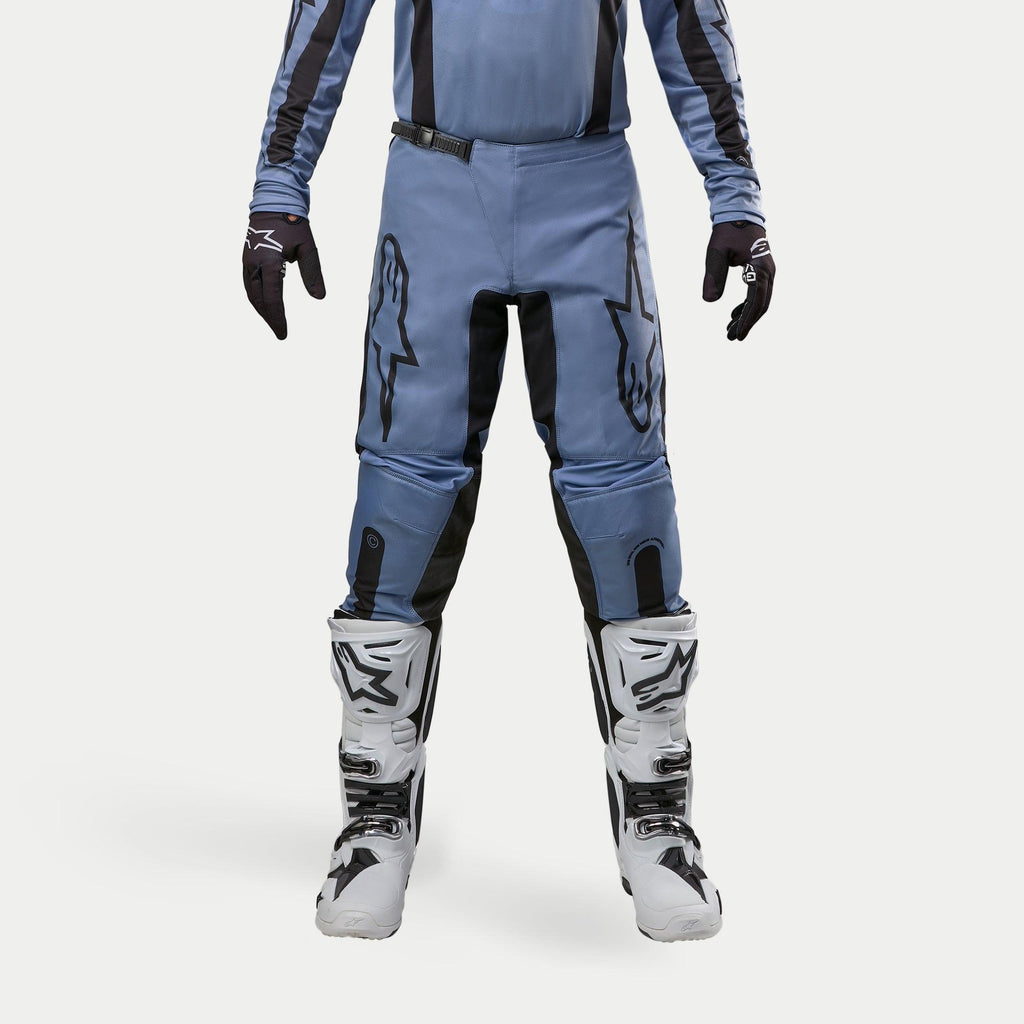 Pantalon Alpinestars Fluid Lurv 2024, pantalon de motocross, bleu clair et noir, porté avec des bottes de course blanches et noires et des gants assortis, arborant des logos étoiles noirs sur les cuisses, conception ergonomique pour la performance tout-terrain