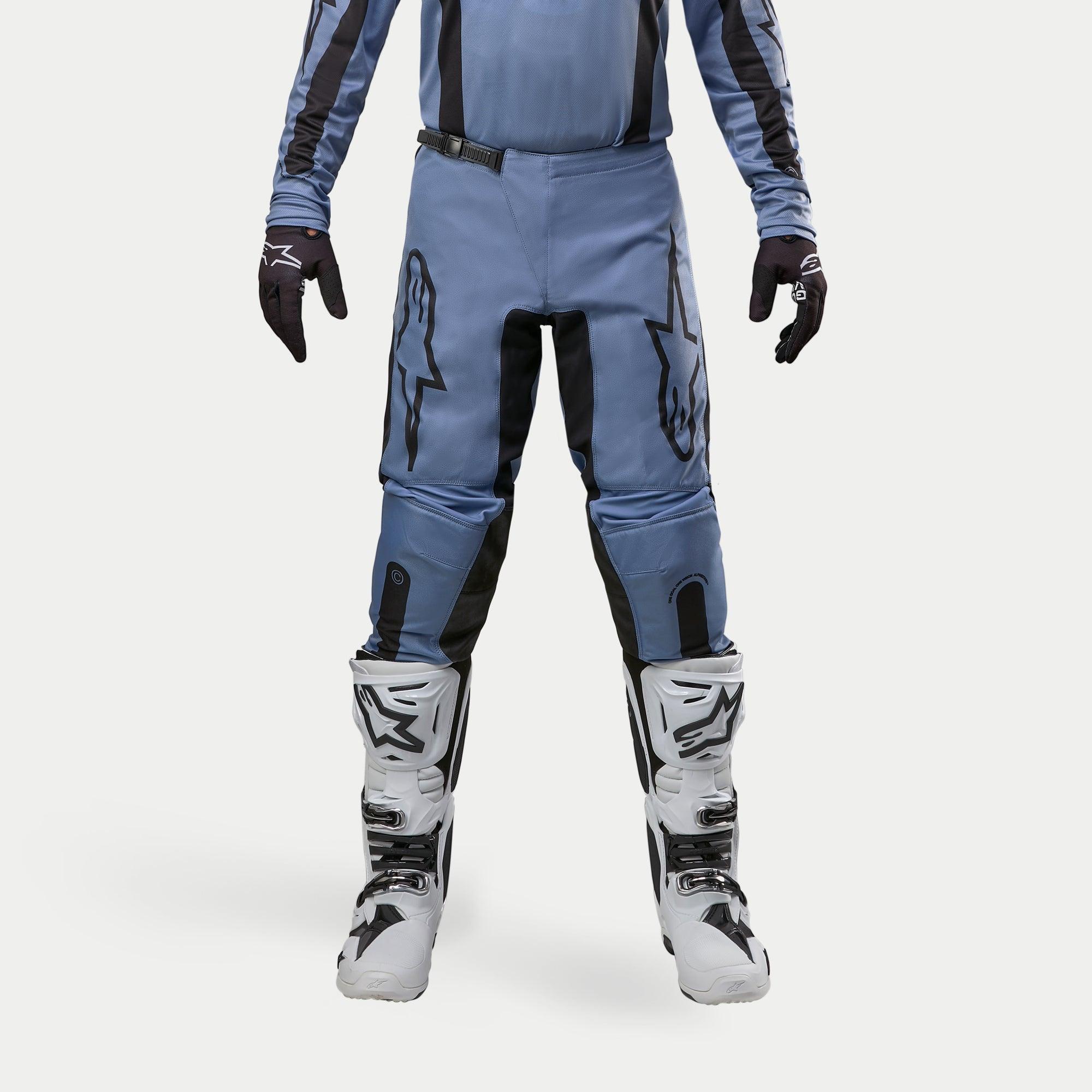 Pantalon Alpinestars Fluid Lurv 2024, pantalon de motocross, bleu clair et noir, porté avec des bottes de course blanches et noires et des gants assortis, arborant des logos étoiles noirs sur les cuisses, conception ergonomique pour la performance tout-terrain