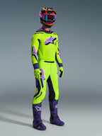 Alpinestars 2026 Supertech Vista Gear Set, professional motocross rider wearing a vibrant lime green jersey and pants with purple accents and logos, matching lime green gloves, purple boots, and a multi-colored helmet with blue goggles, coordinated athletic-fit gear for off-road racing