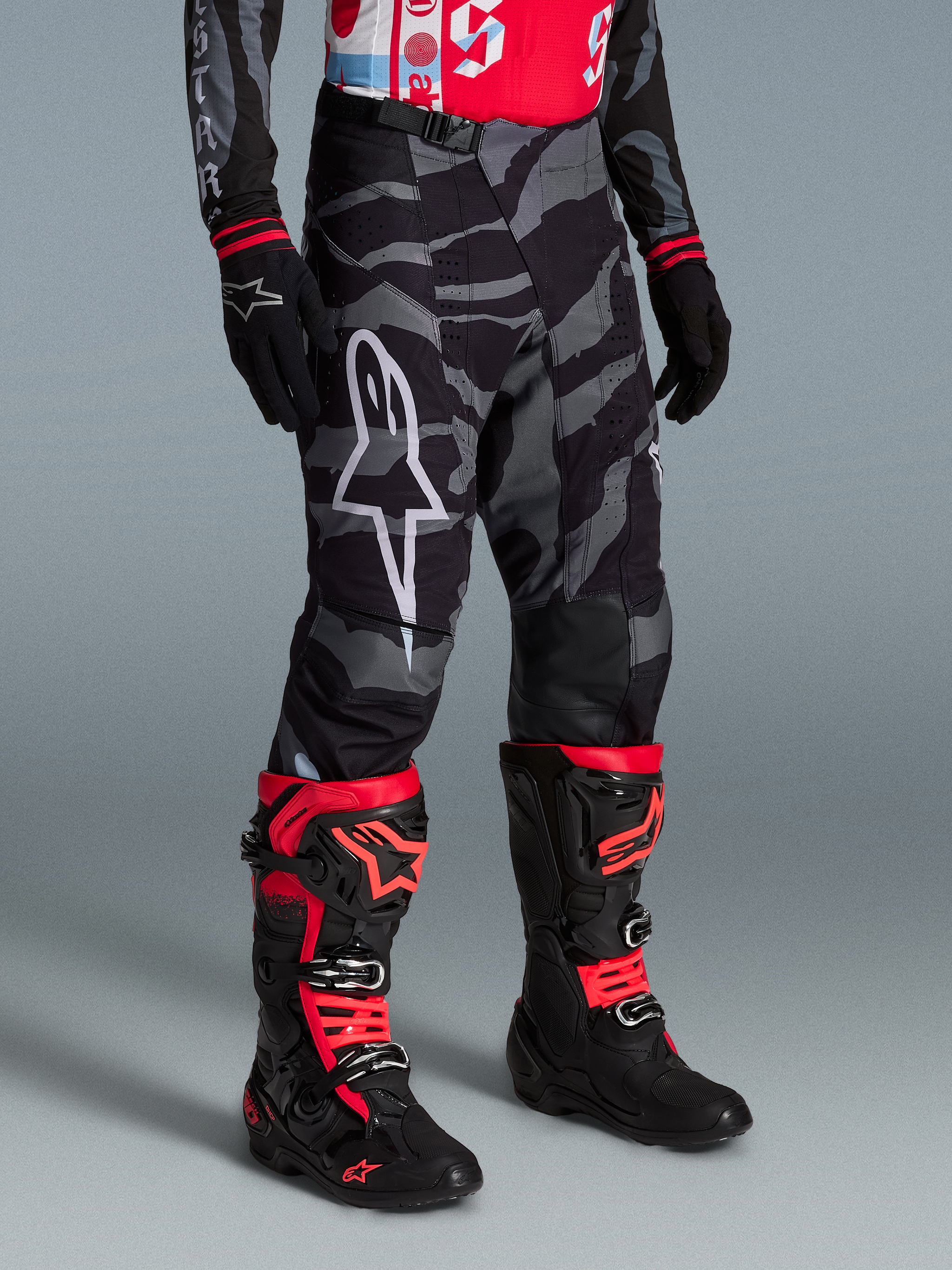 Pantalon Techstar Beast Coast, camouflage gris et noir, logo blanc, porté avec des bottes de motocross rouges et noires.