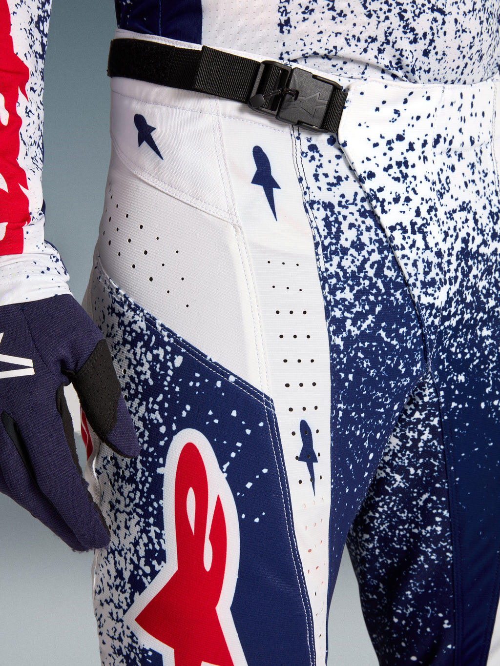 Pantalons de motocross Alpinestars Techstar Unity pour homme, bleu, blanc et rouge, avec boucle magnétique SX2 et perforations laser, vue rapprochée des détails.