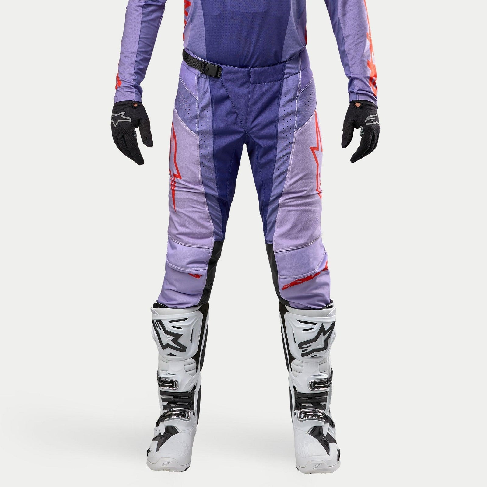 Alpinestars 2024 Techstar Ocuri Pants, pantalon de motocross, violet avec accents orange vif et logos rouges, porté avec des bottes de motocross blanches et des gants noirs, équipement technique durable.