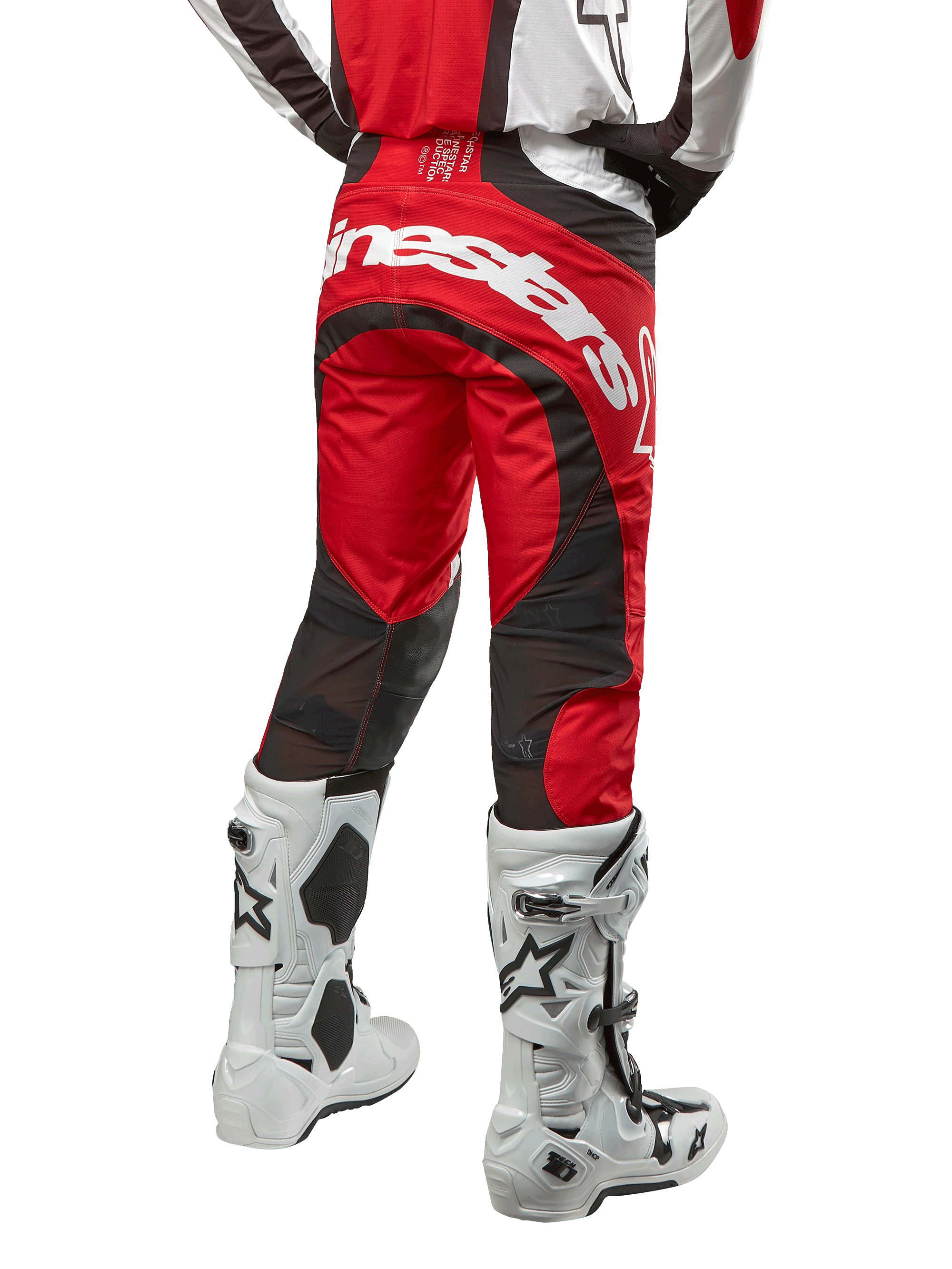 Pantalon Alpinestars Techstar Ocuri 2024, pantalon de motocross, rouge Mars, blanc et noir, vue arrière avec grand logo Alpinestars blanc sur l'assise, panneaux de ventilation en mesh noir, porté avec des bottes de motocross blanches et noires, coupe athlétique pour le pilotage tout-terrain