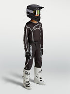 Alpinestars Jeugd Fluid Apex V2 broek, zwart en zilver motocrossuitrusting op model met jersey, helm en witte motorlaarzen.