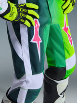 Alpinestars 2026 Jugend-Fluid Portl Hose, Motocross-Hose, Grün, Weiß und Schwarz mit pinkfarbenen Stern-Logos, Nahaufnahme von strapazierfähigem 600D-Polygewebe und weißen Einsätzen, getragen mit neongelben Handschuhen und Offroad-Stiefeln