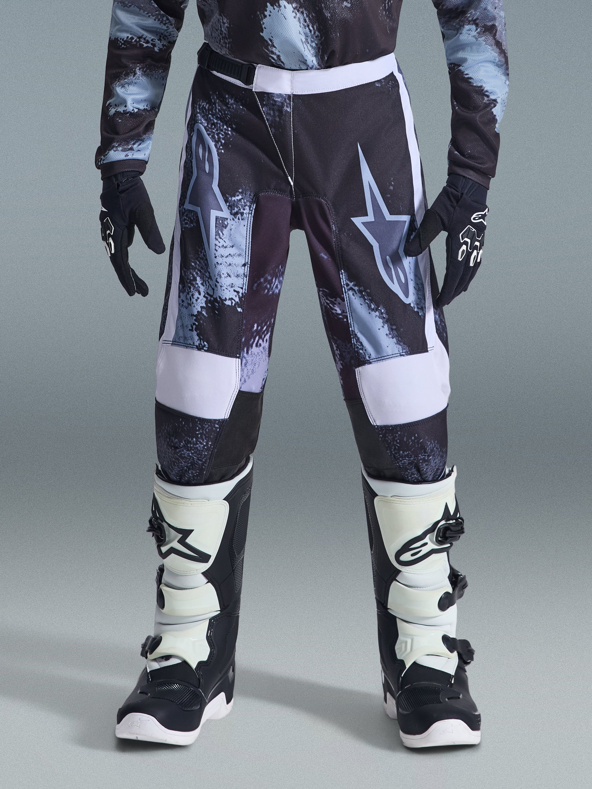 Alpinestars Youth Fluid Lahnd Pants 2026, jeugd motorcrossbroek, Iron Camo met witte accenten, gedragen met zwart-witte off-road laarzen en handschoenen, duurzaam ontwerp voor jonge rijders.