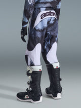 Alpinestars 2026 Youth Fluid Lahnd Pants, motorcrossbroek, Iron Camo met witte accenten, achteraanzicht met 'astars' logo op het zitvlak, gedragen met bijpassend camo shirt en zwart-witte Tech 3 motorcrosslaarzen.