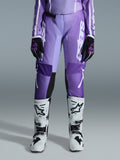 Alpinestars Stella Fluid Apex 2026 pour femme, pantalon de motocross, violet et blanc, porté avec des gants noirs et violets et des bottes blanches et noires, avec logo blanc audacieux sur la jambe, design ergonomique sport-fit pour la course tout-terrain