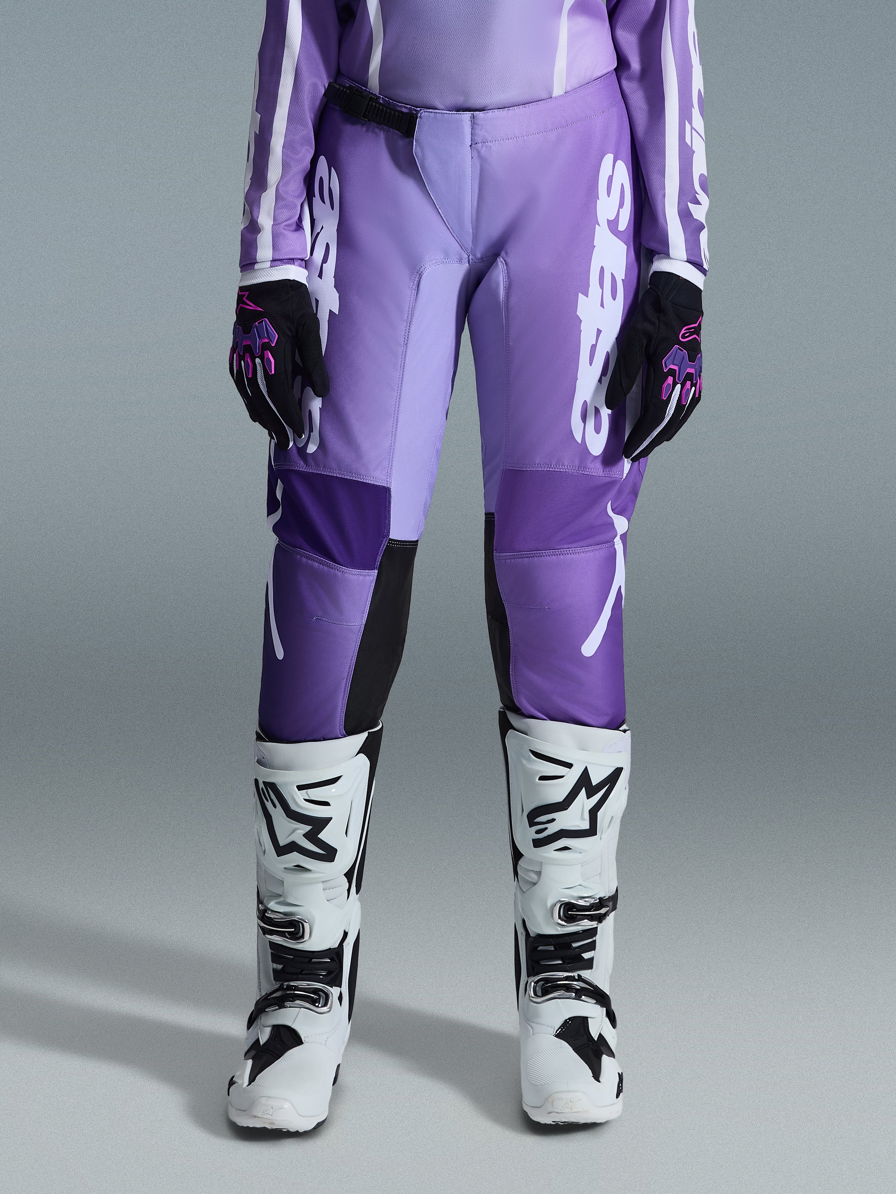 Alpinestars 2026 Stella Fluid Apex Damen-Hose, Motocross-Hose, Violett und Weiß, kombiniert mit schwarz-violetten Handschuhen und weiß-schwarzen Stiefeln, mit markantem weißem Branding am Bein, ergonomisches Sport-Fit-Design für Offroad-Rennsport