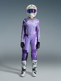 Motocrossrijder in de Alpinestars 2026 Stella Fluid Apex Gear Set voor dames, violette en witte jersey met bijpassende broek, witte helm met roze bril en witte en zwarte off-road laarzen, complete race-uitrusting voor dames motocross.