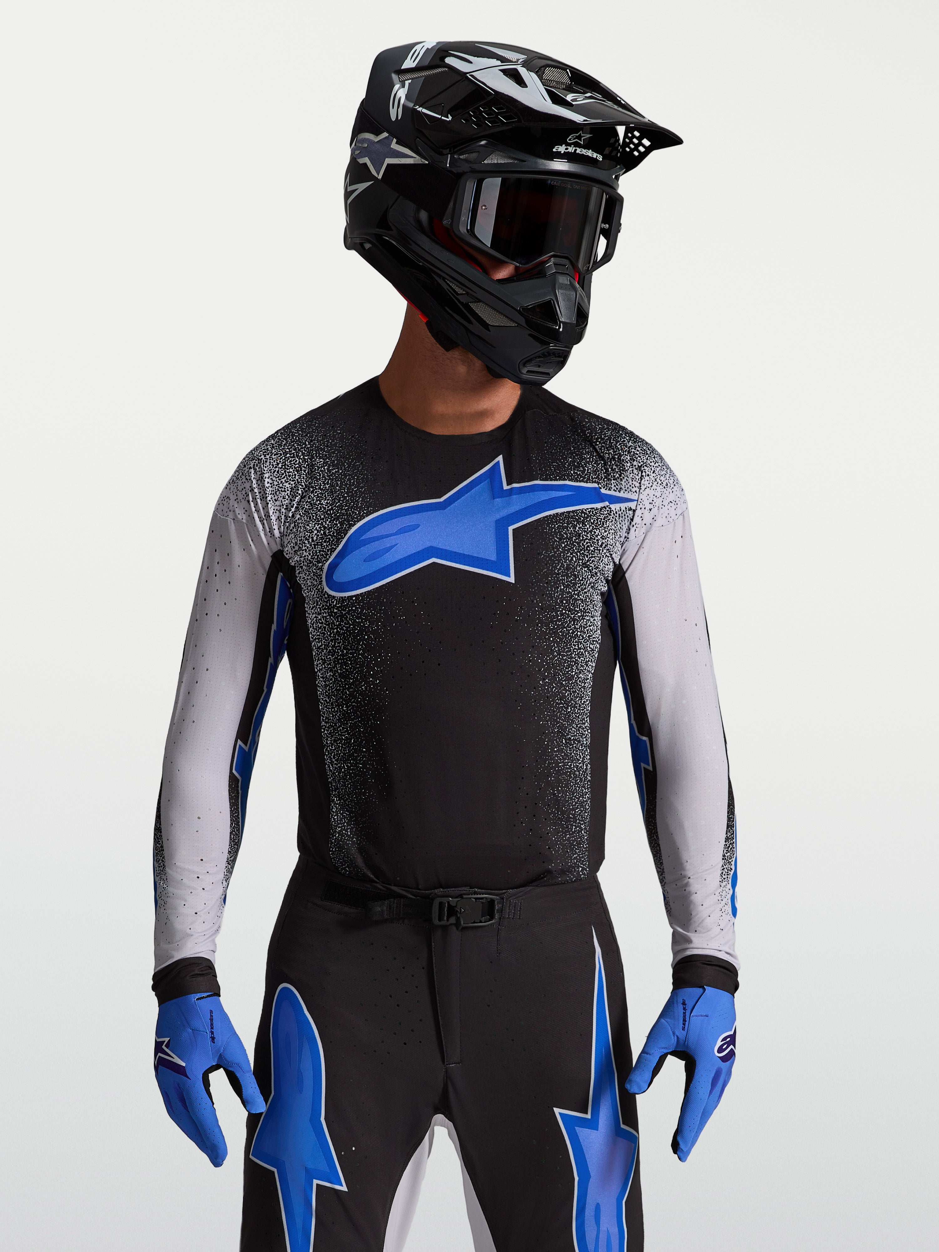 Maillot Supertech Hiten AFD Alpinestars, maillot de motocross pour homme, noir et bleu, technologie de protection AFD, coupe racing athlétique, porté par un mannequin avec casque et gants de moto