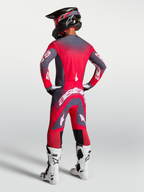 Alpinestars Supertech Hiten AFD Jersey en Gear Set, professionele motocross-uitrusting, rood en grijs, achteraanzicht van model met helm en witte motorlaarzen.