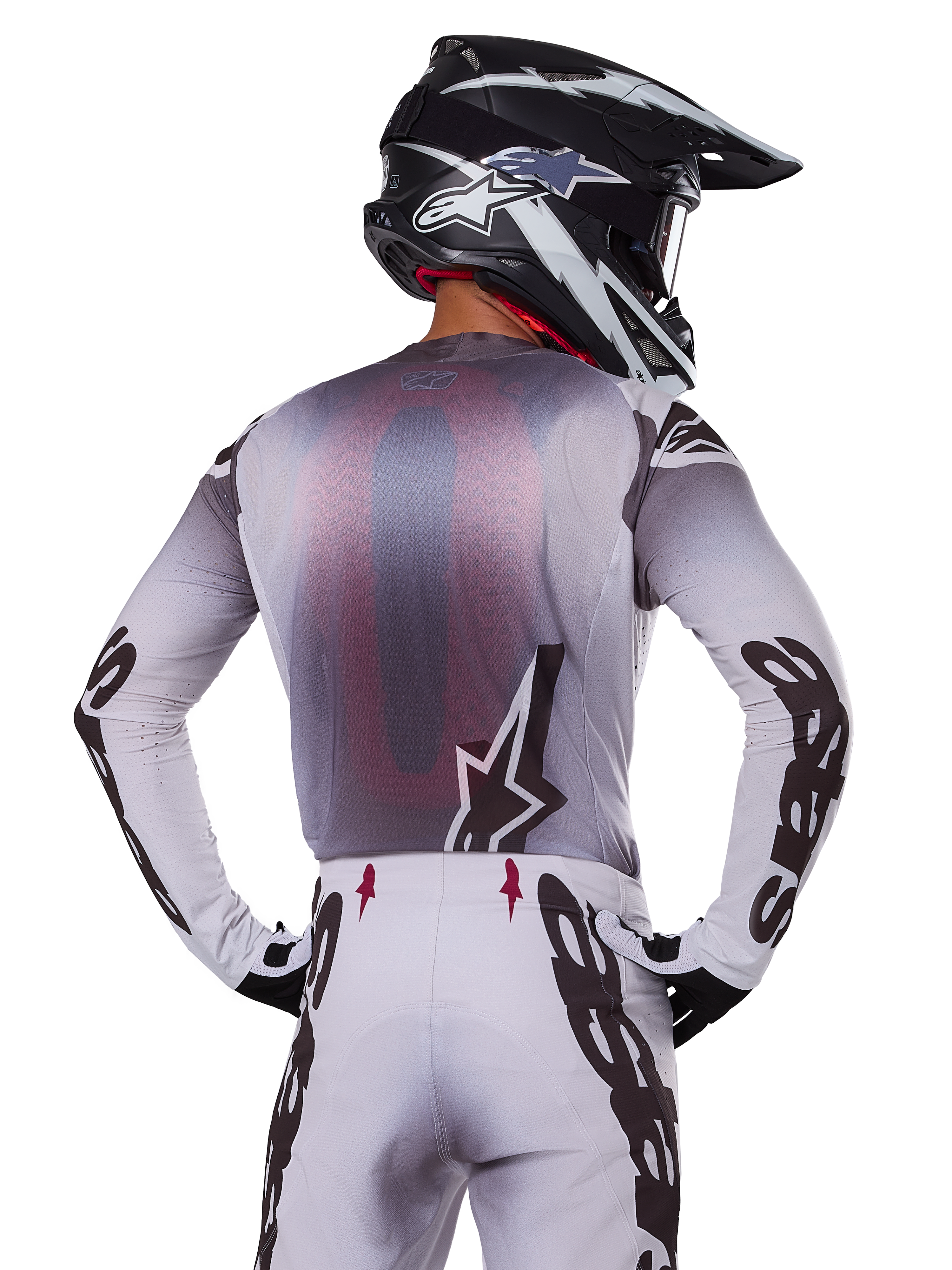 Motocrosser van achteren die de Alpinestars 2025 Supertech Maker Jersey draagt, zilver en zwart met een rood mesh rugpaneel en zwarte logo's op de mouwen, gecombineerd met een bijpassende motorcrossbroek en een zwart-witte helm, professionele off-road race-uitrusting