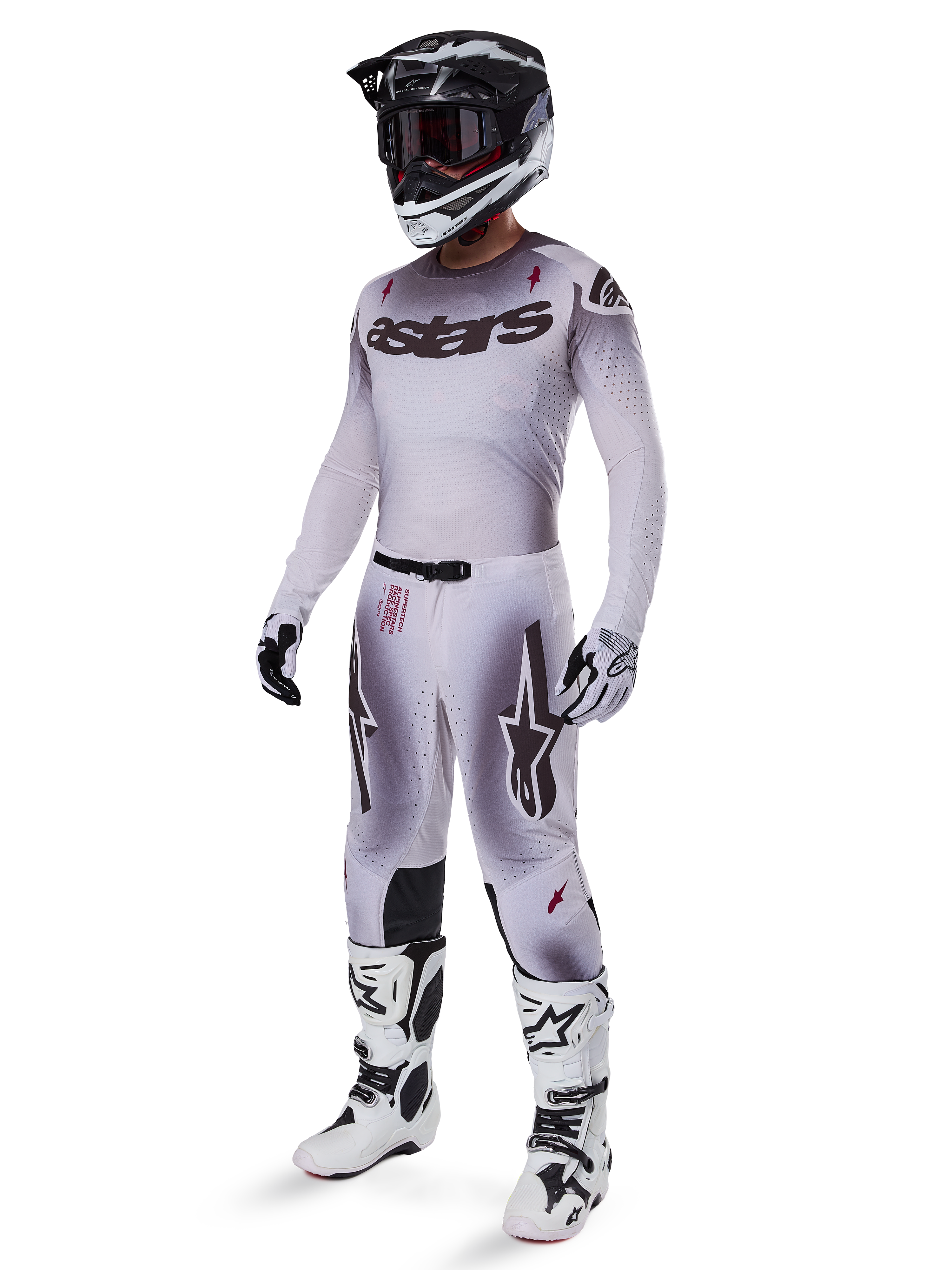 Motorcrossrijder die de Alpinestars 2025 Supertech Maker Jersey in zilver en zwart draagt, met bijpassende zilveren en zwarte broek, zwart-witte helm met zwarte crossbril, witte en zwarte laarzen en bijbehorende handschoenen, professioneel verloopontwerp voor off-road racing