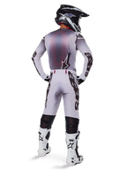 Motocross rider from behind wearing Alpinestars 2025 Supertech Maker Pants in Silver and Black, matching long-sleeve jersey, black and white helmet, and white and black boots, featuring bold black branding on the legs, professional off-road racing gear.