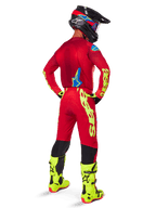 Motocross-Fahrer in der Rückansicht mit dem Alpinestars 2025 Supertech Maker Gear Set, leuchtend rotes Trikot mit neongelbem Branding, passende rote Hose mit gelben Akzenten, schwarzer Helm mit roten und blauen Details, neongelbe Stiefel, abgestimmtes professionelles Rennoutfit für Offroad-Performance.