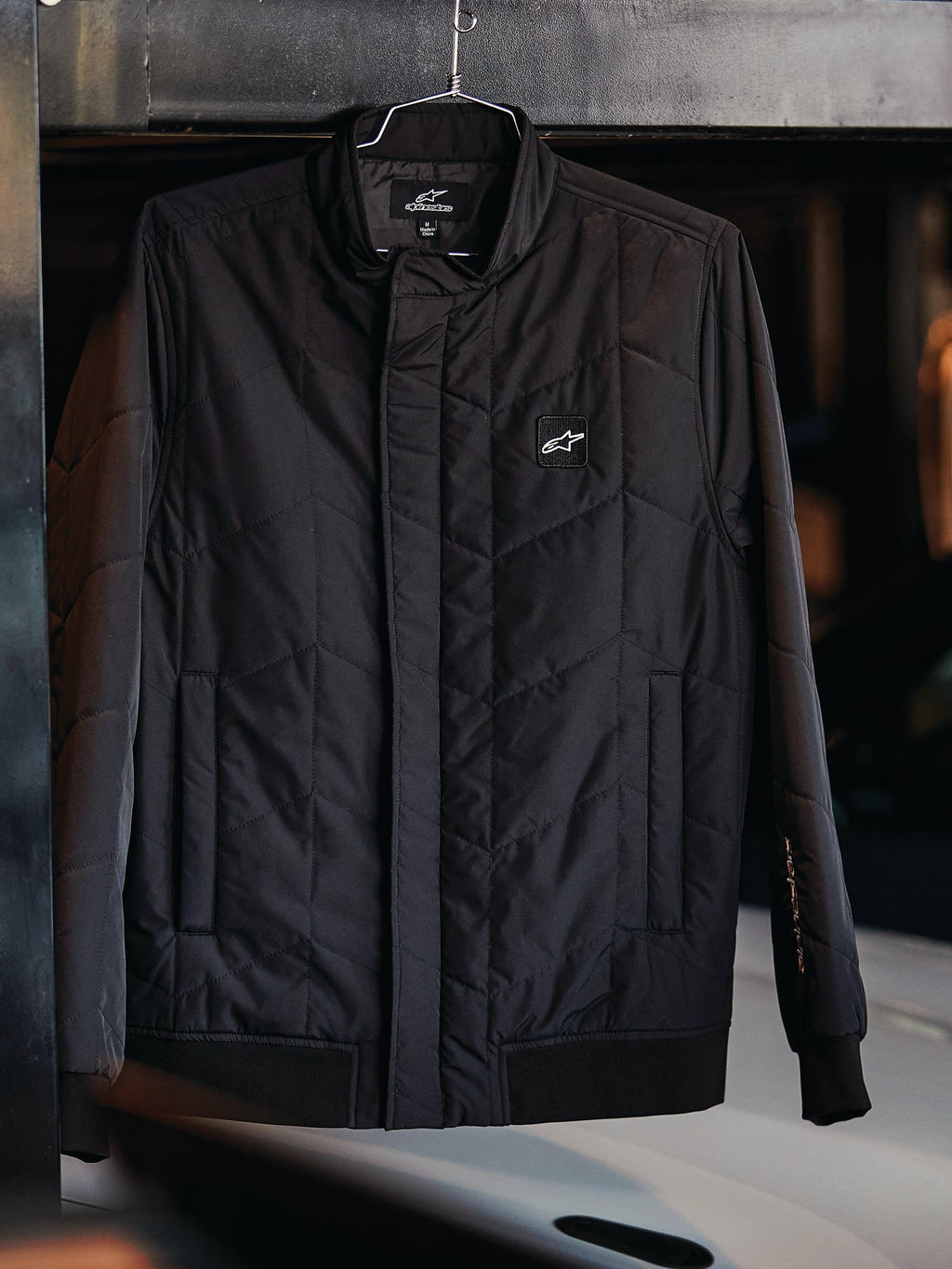 Alpinestars Precedent Jas, gestept sportjack, zwart, voorzien van een schuin doorgestikt patroon, lage kraag met bedekte rits, logopatch op de borst en geribde manchetten en zoom, op motorsport geïnspireerd design